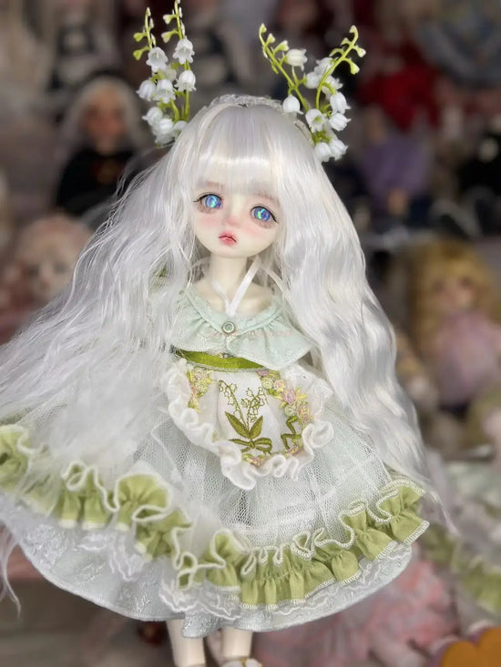 6 niveltä prinsessanukke meikillä with long white hair and floral accents wearing a delicate green and white dress.